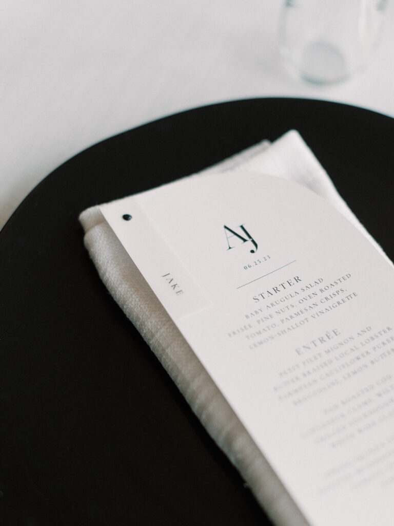 Custom black and white wedding menu styled on black charger with napkin