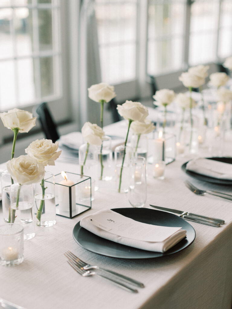 Reception tablescape with single white roses, candles, and black chargers