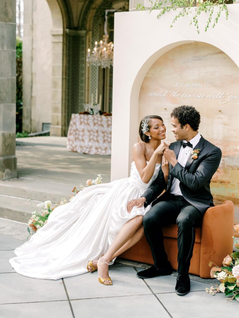 Bride and groom sharing a moment on a terracotta lounge with a romantic arch backdrop
