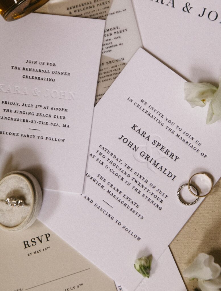 Close-up of wedding invitation featuring classic letterpress and wedding rings on cream linen backdrop.