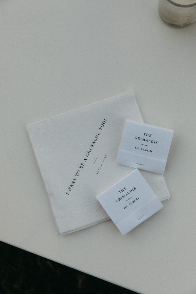 Stack of white custom wedding napkins and matchbooks featuring a minimalist black monogram for Kara and John’s Crane Estate wedding