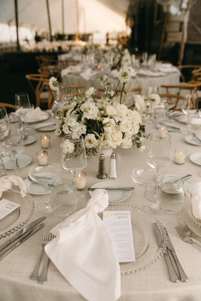 Elegant wedding reception table with white florals, clear chargers, and wax-sealed menus at Crane Estate