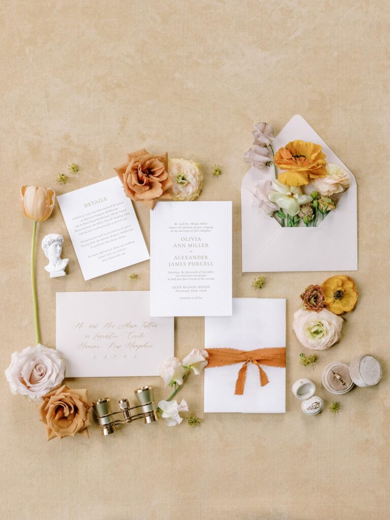 Flat lay of a romantic fall wedding invitation suite with fresh flowers and rust silk ribbon