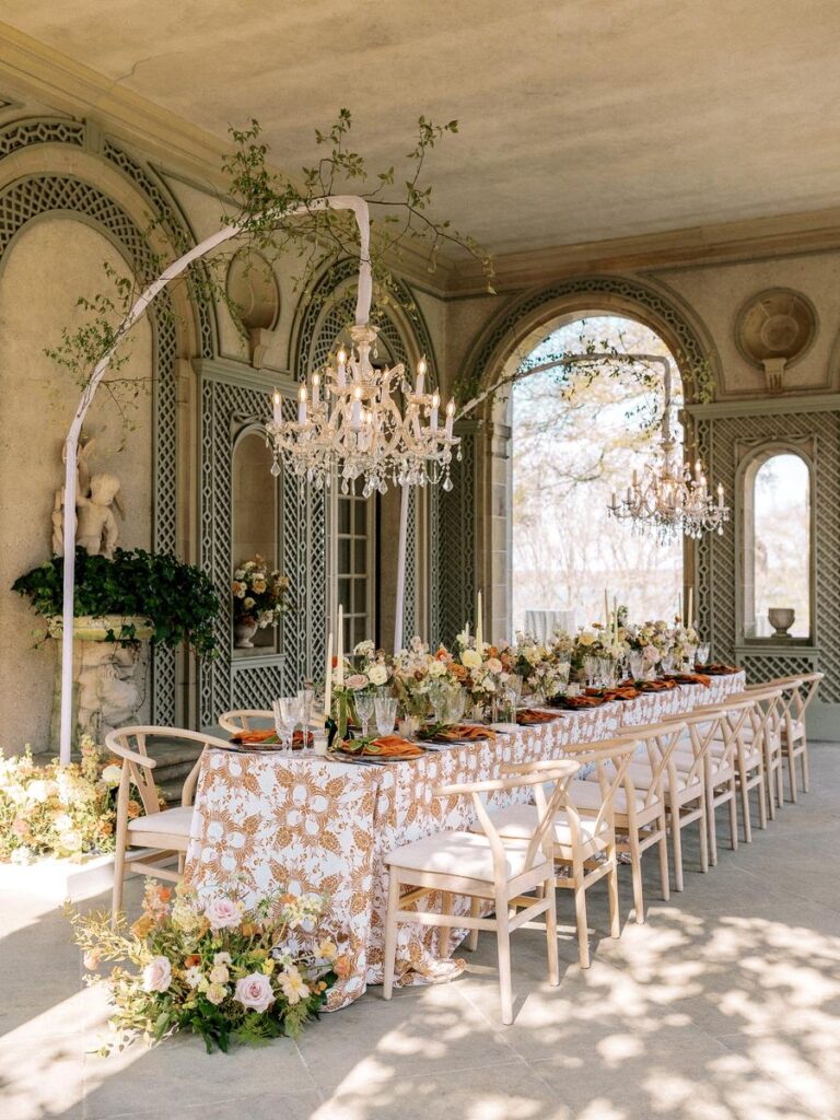 Full view of a romantic wedding reception tablescape with floral centerpieces, rust linens, and chandeliers