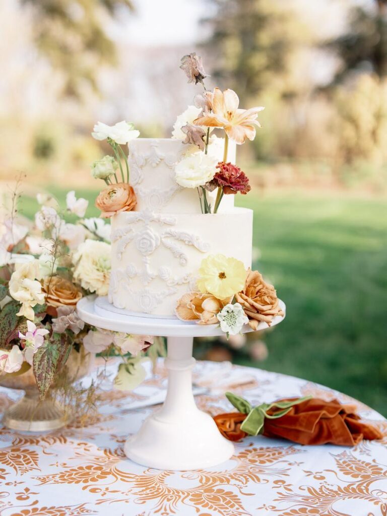 Romantic two-tier white wedding cake decorated with fresh florals on a patterned garden table
