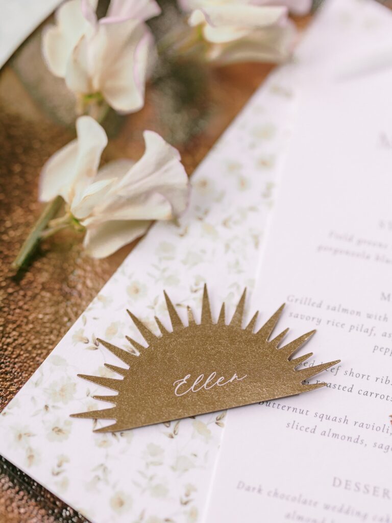 Custom sunburst place card on top of a floral menu with blush sweet pea flowers