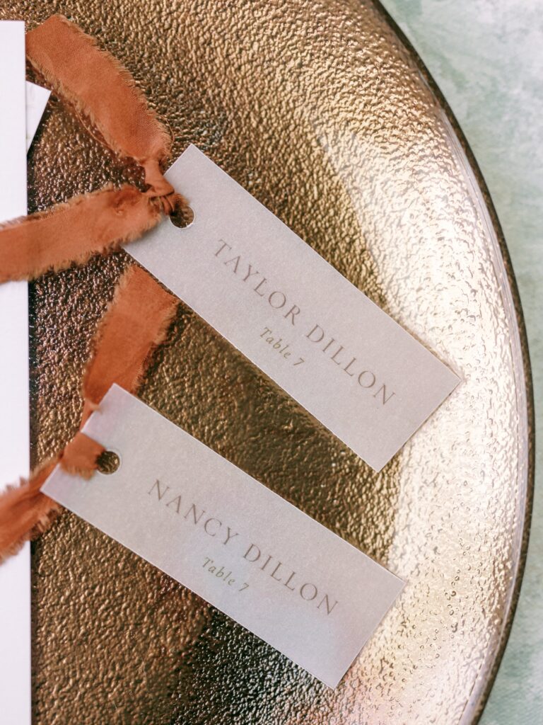 Vellum escort cards with rust silk ribbon displayed on a metallic charger for a romantic wedding