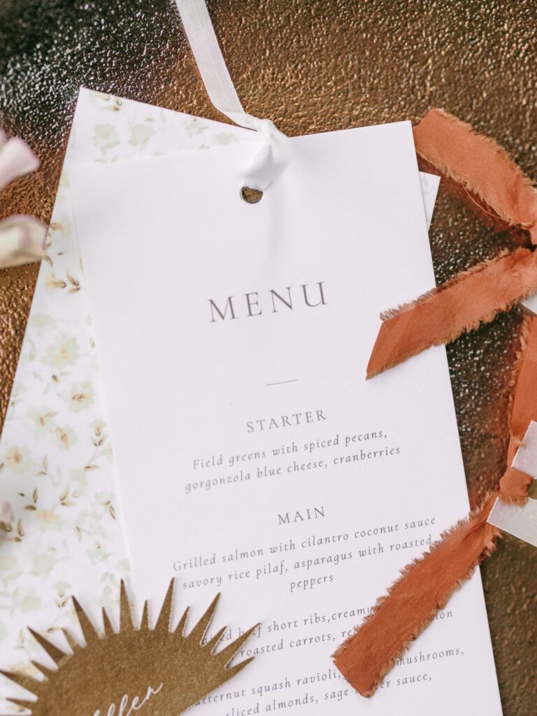 Elegant wedding menu card with delicate typography, floral backing, and silk ribbon detail.